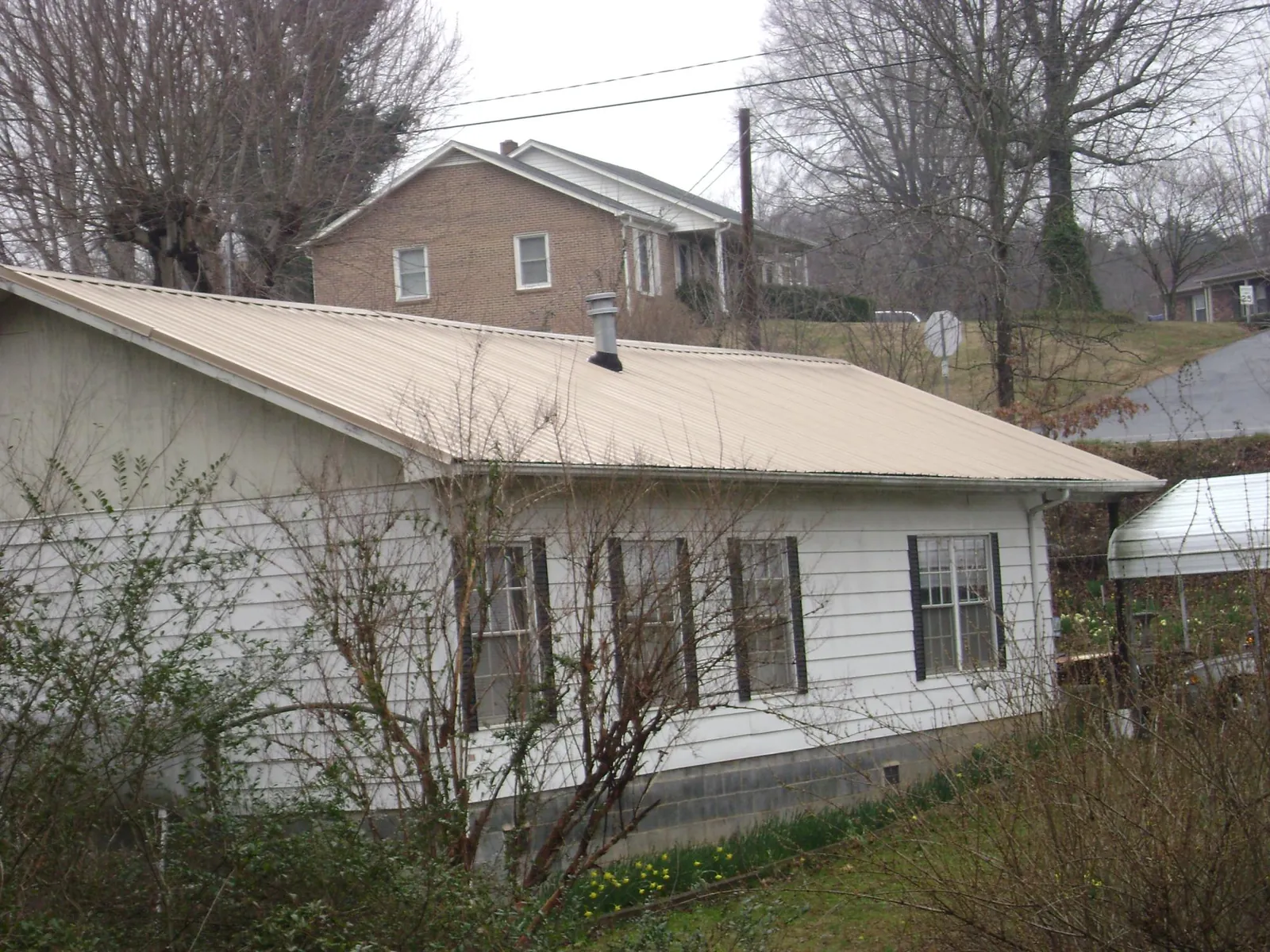 Tan metal roof on a white sided house set into a hillside — Commercial Roofing by Roofing Brothers in Warrenton